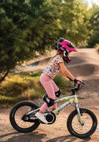 Niña con casco rosa pedaleando una bicicleta en un sendero de tierra.