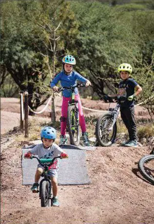 Tres niños con casco y bicicleta en una pista de tierra.
