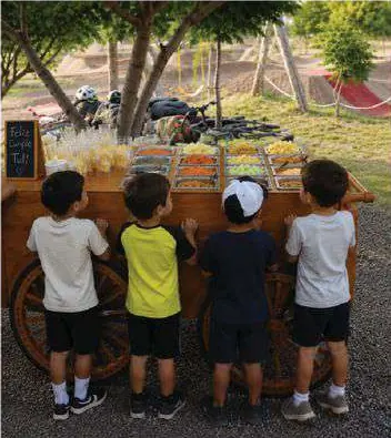 Cuatro niños de espaldas frente a un carrito de botanas al aire libre.