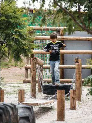 Niño de pie en una estructura de troncos, llantas y cuerdas.