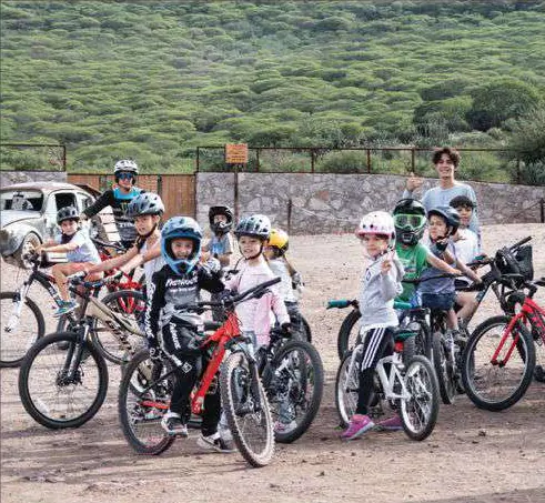 Grupo de niños con casco y bicicletas, frente a un cerro verde.