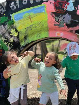 Dos niñas frente a un arco de llantas pintadas de colores.