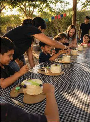 Niños y adultos decorando pasteles pequeños en una mesa al aire libre.