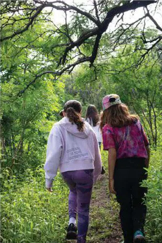 Tres personas caminando de espaldas por un sendero entre árboles.